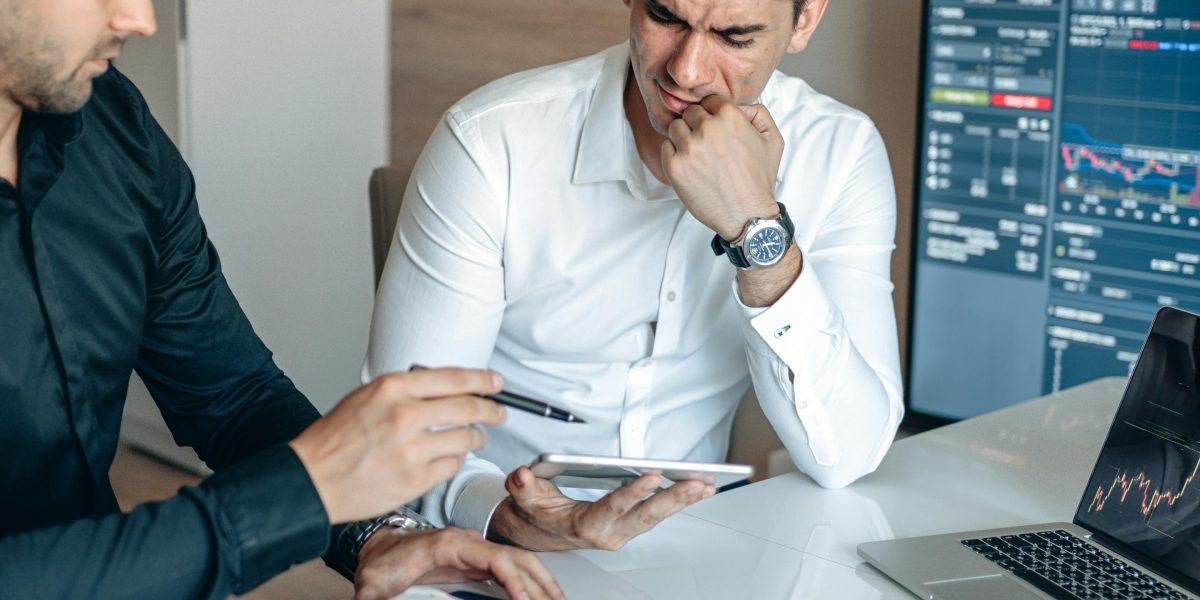 Two business professionals engaged in a discussion, perhaps reviewing different hosting plans or business strategies on a tablet or whiteboard.