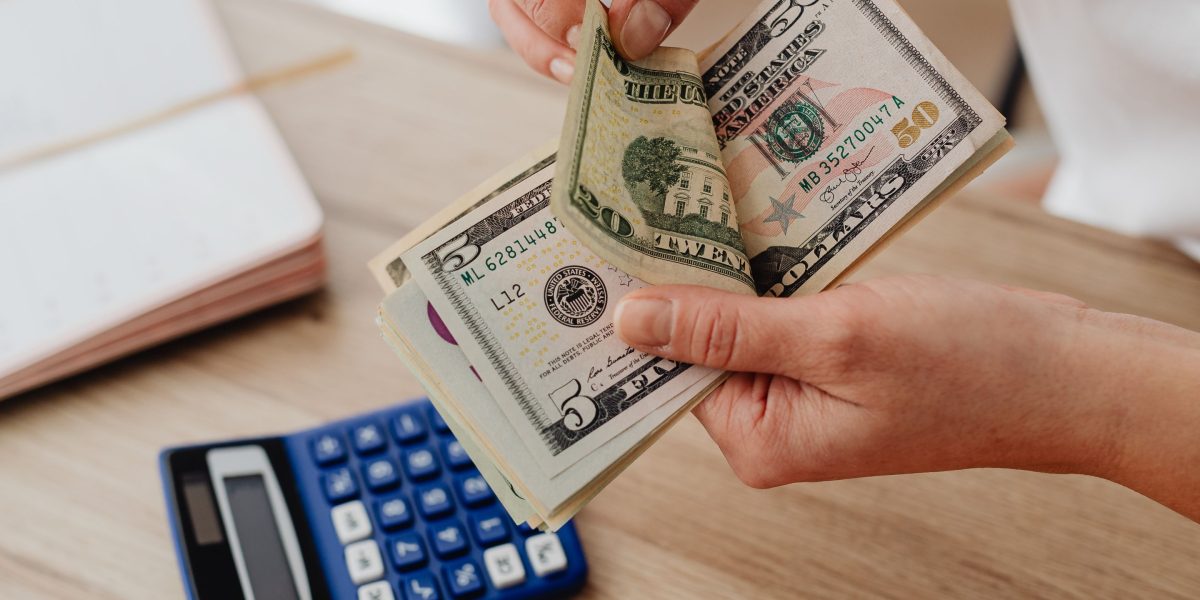 An individual diligently calculates potential monthly website expenses, using a pen and notebook.